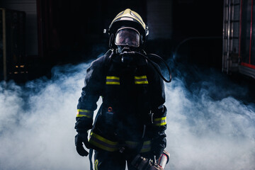 Portrait of a female firefighter wearing a helmet and all safety equipment a while holding a...