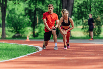 Young couple stretching before starting their morning jogging routine on a tartan track at the park.