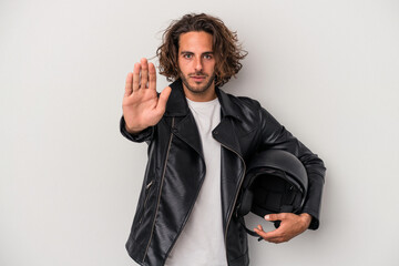 Young biker caucasian man holding a motorbike helmet isolated on gray background standing with...