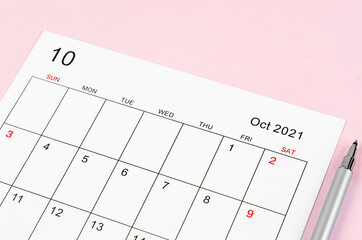 October 2021 calendar sheet with pen on pink background.