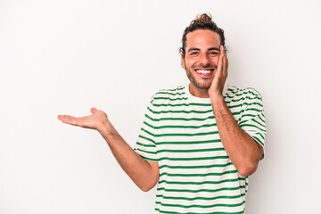 Young caucasian man isolated on white background holds copy space on a palm, keep hand over cheek. Amazed and delighted.