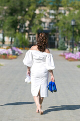 A bride without shoes in a white dress with a bouquet of flowers and blue shoes in her hands is walking around the city.