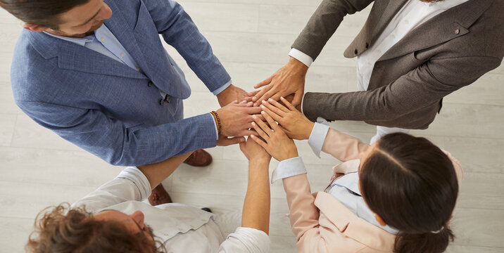 Close up top view of diverse employees workers stack hands in pile engaged in teambuilding activity together. Multiracial colleagues feel motivated for shared business success or goal achievement.