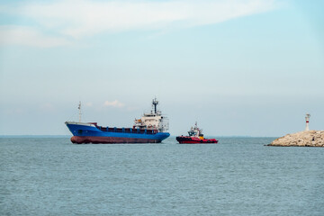 A cargo ship leaving the port with a guide