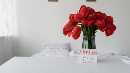Happy Valentine's Day bouquet of red tulips in a glass vase romantic holiday atmosphere in the morning in the bedroom. Flowers for the beloved