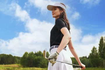 Gordijnen Professional female golfer holding golf club on field and looking away. Young woman standing on golf course on a sunny day. © ty