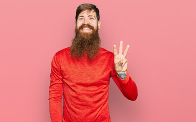 Redhead man with long beard wearing casual clothes showing and pointing up with fingers number three while smiling confident and happy.