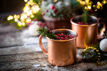 Mulled wine with cranberry in copper mug with christmas decorations on wooden table