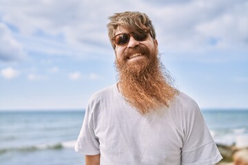 Fototapeta na wymiar Young redhead tourist man smiling happy standing at the beach.