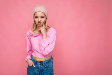 Photo of beautiful happy funny young blonde woman isolated over pink background wall wearing trendy pink hat and pink blouse looking at camera and having fun