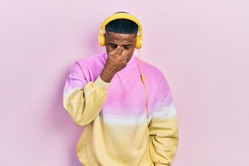Young black man listening to music wearing headphones tired rubbing nose and eyes feeling fatigue and headache. stress and frustration concept.