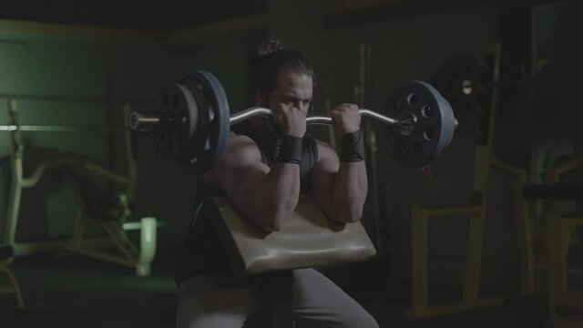 S-Log. professional bodybuilder working out in the indoor gym. weight lifting and bodybuilding, muscle strengthening workout. man doing biceps curl exercise on barbell with heavy plates. fitness