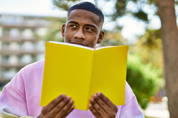 Young african american man smiling happy reading book at the city.