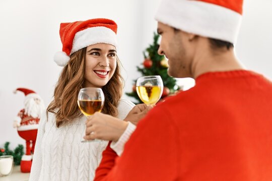 Young hispanic couple wearing christmas hat toasting with champagne at home.