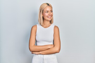 Beautiful blonde woman wearing casual style with sleeveless shirt looking away to side with smile on face, natural expression. laughing confident.