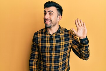 Young hispanic man wearing casual clothes waiving saying hello happy and smiling, friendly welcome gesture