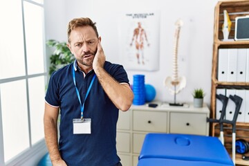 Middle age physiotherapist man working at pain recovery clinic touching mouth with hand with painful expression because of toothache or dental illness on teeth. dentist