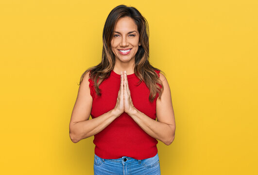 Young hispanic woman wearing casual clothes praying with hands together asking for forgiveness smiling confident.