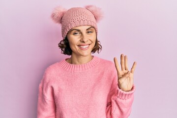 Young brunette woman wearing cute wool cap showing and pointing up with fingers number four while smiling confident and happy.