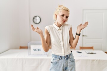 Beautiful caucasian woman standing by voting ballot at election room clueless and confused...