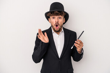 Young arab wizard man holding a wand isolated on white background surprised and shocked.