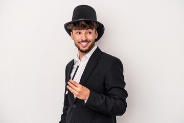 Young arab wizard man holding a wand isolated on white background looks aside smiling, cheerful and pleasant.