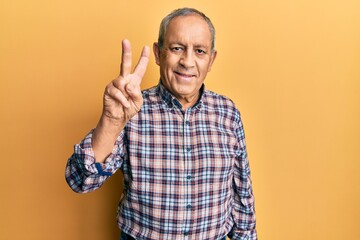 Fototapeta premium Handsome senior man with grey hair wearing casual shirt showing and pointing up with fingers number two while smiling confident and happy.