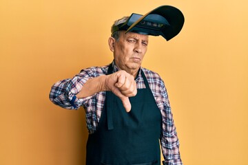 Handsome senior man with grey hair wearing welding protection mask looking unhappy and angry...