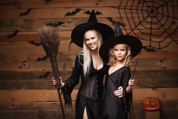 Halloween Concept - cheerful mother and her daughter in witch costumes celebrating Halloween posing...