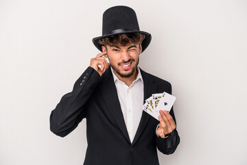 Young arab wizard man holding a magic cards isolated on white background covering ears with hands.