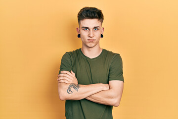 Young caucasian boy with ears dilation wearing casual green t shirt skeptic and nervous, disapproving expression on face with crossed arms. negative person.
