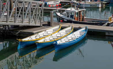 Fototapeta na wymiar Newlyn Harbour, Cornwall, England, UK. 2021. Three pilot gig boats on a jetty in Newlynn Harbour.
