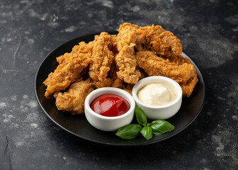 Fried Chicken strips with ketchup and mayonnaise on black plate. Fast Food