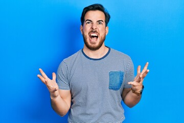 Fototapeta premium Handsome caucasian man with beard wearing casual striped t shirt crazy and mad shouting and yelling with aggressive expression and arms raised. frustration concept.
