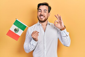 Handsome caucasian man with beard holding mexican hat doing ok sign with fingers, smiling friendly...