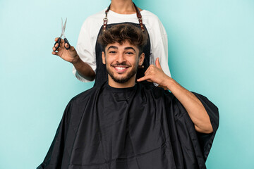 Young arab man ready to get a haircut isolated on blue background showing a mobile phone call...