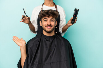 Young arab man ready to get a haircut isolated on blue background showing a copy space on a palm...