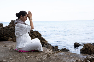 A beautiful pregnant young woman is meditating on the beach	