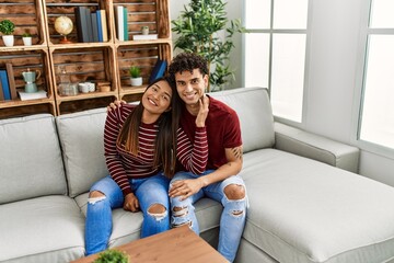 Obraz premium Young latin couple smiling happy and hugging sitting on the sofa at home.