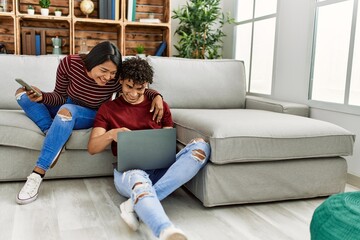 Obraz premium Young latin couple smiling happy using laptop and smartphone at home.