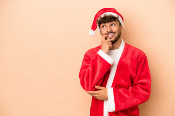Young arab man disguised as santa claus isolated on beige background relaxed thinking about something looking at a copy space.