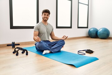 Young hispanic sporty man smiling happy training yoga at sport center.