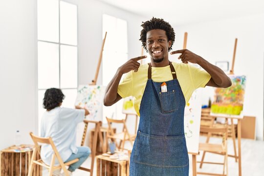 African young man standing at art studio smiling cheerful showing and pointing with fingers teeth and mouth. dental health concept.