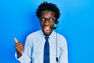 Young african american man wearing call center agent headset pointing thumb up to the side smiling happy with open mouth