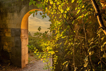 A look through a marl stone gate with a view on the vineyards and a golden colored sunrise on a misty morning in October  on the hills just outside Maastricht.