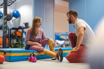Woman with prosthetic legs talking to a trainer while doing physiotherapy
