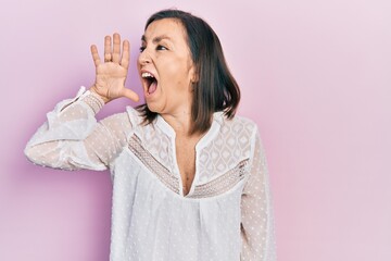 Middle age hispanic woman wearing casual clothes shouting and screaming loud to side with hand on mouth. communication concept.