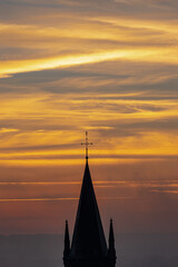 Fototapeta premium A typical colorful Autumn sunrise in Maastricht with the landscape covered with a layer of fog, leaving only silhouettes visible in the distance, like this tower of a church on the hillside.