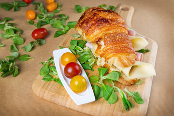 Croissant sandwich filled with ham and cheese on wooden chopping board