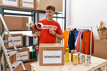 Young caucasian volunteer man packing donations box at charity center smiling happy pointing with...